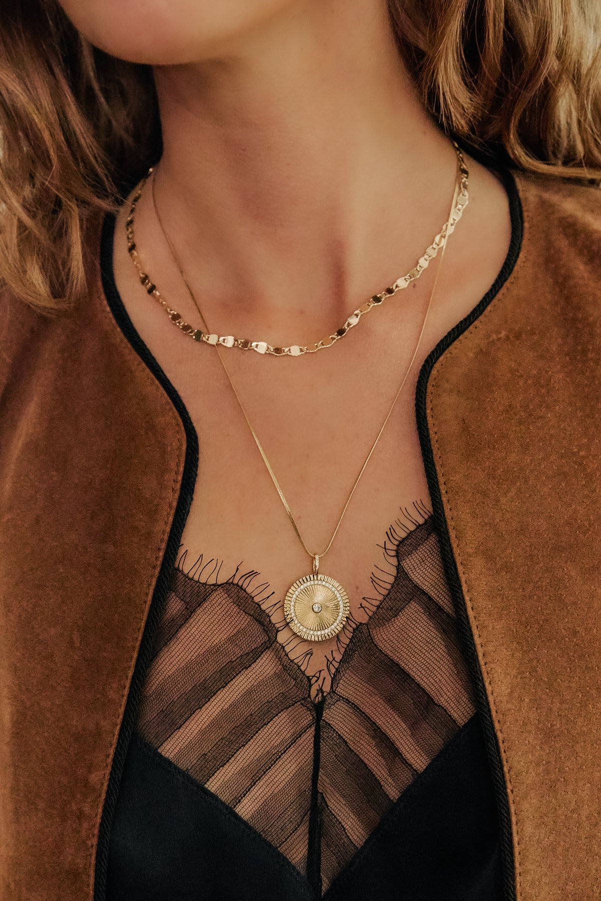 Model wearing gold Ava necklace and Josephine chain with Solara Charm over black lace top and brown jacket.