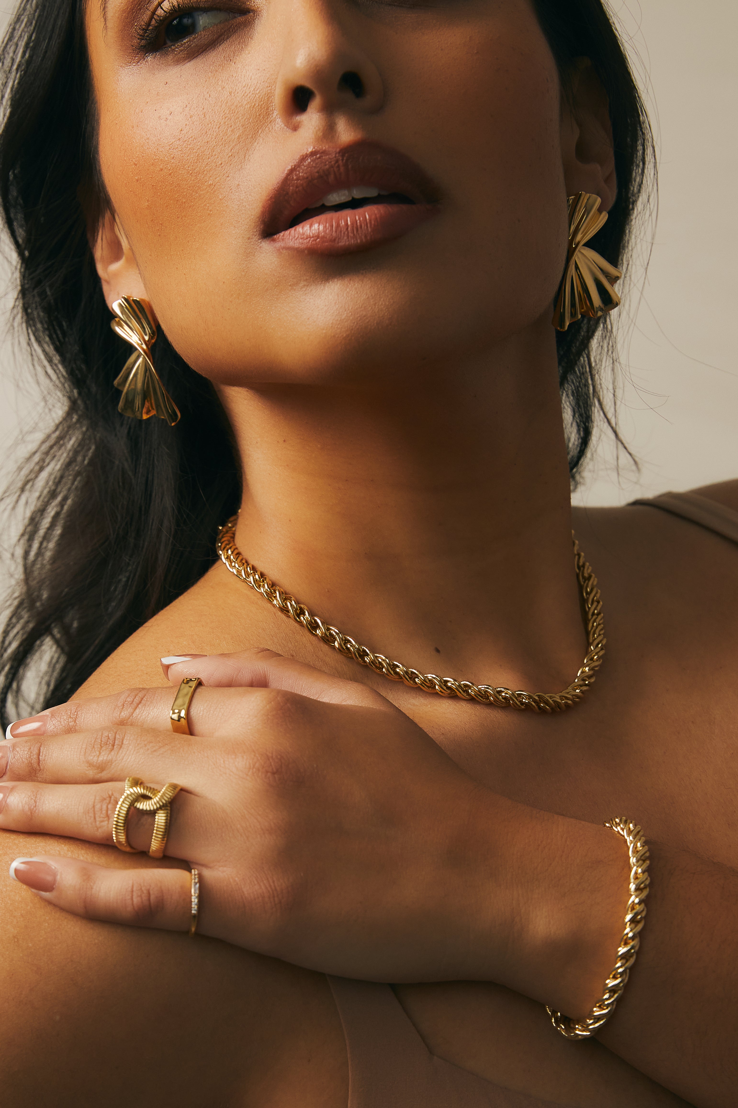 Close-up model photo of a woman wearing Adriana Gold Rope Chain Necklace layered with delicate bracelets, rings and earrings.