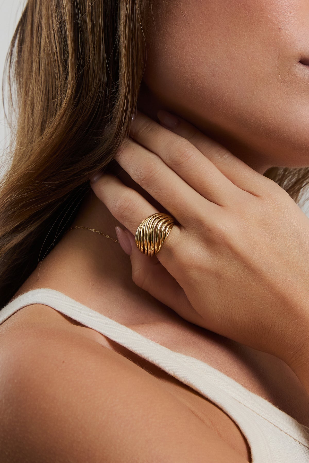 Model wearing gold Etta dome ring on index finger, resting hand near neck in a cream ribbed top.