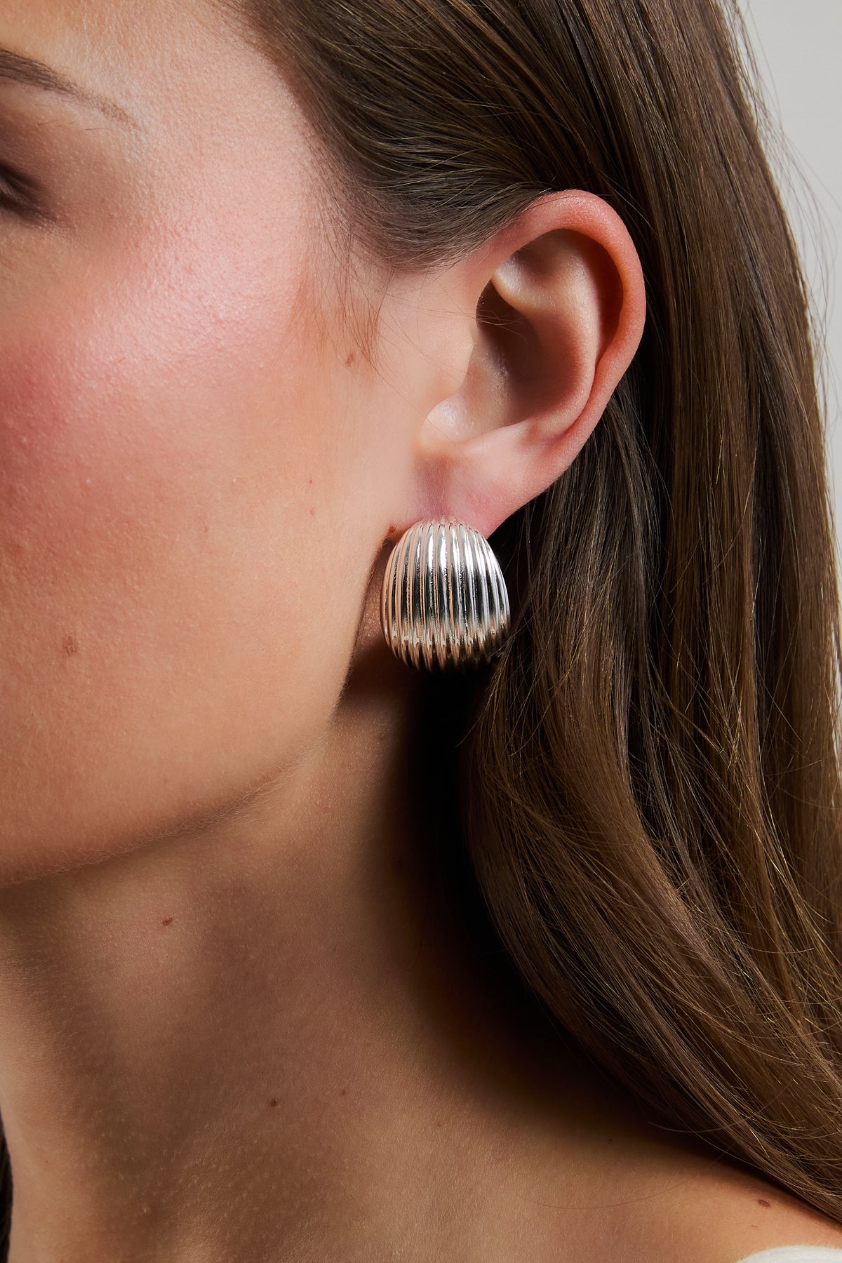 Close-up side profile of model wearing silver Florence ribbed dome hoop earring.