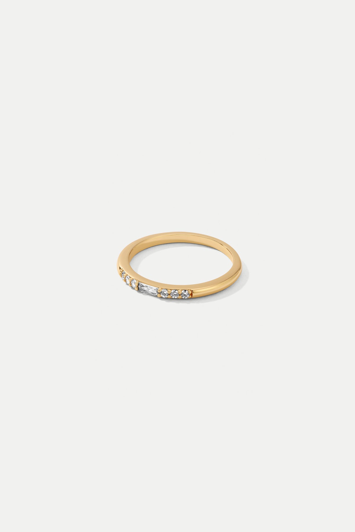 Gold Eve slim band ring set with a baguette CZ centerpiece surrounded by round CZ stones on a white background.