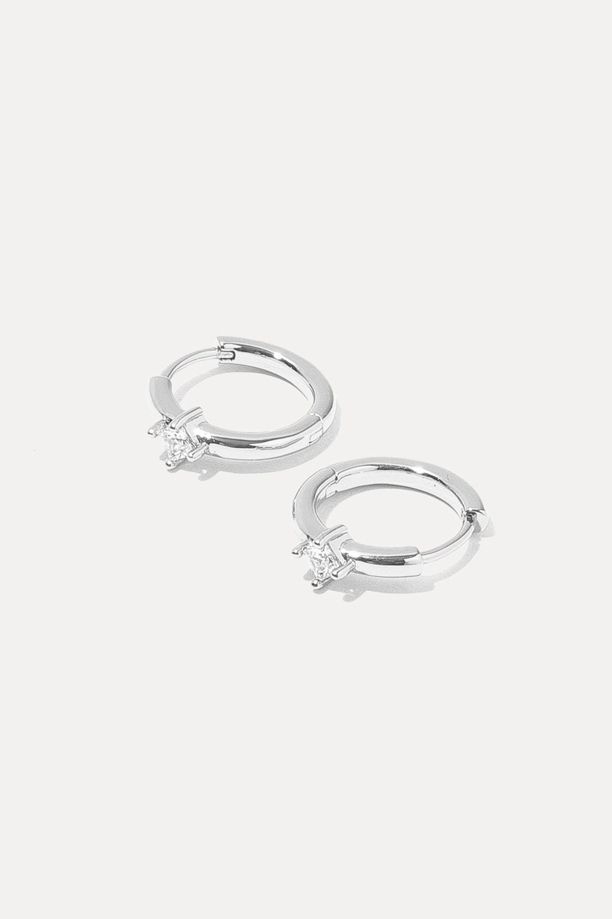 Pair of silver Kierza Huggies with cubic zirconia center stones on a white background.