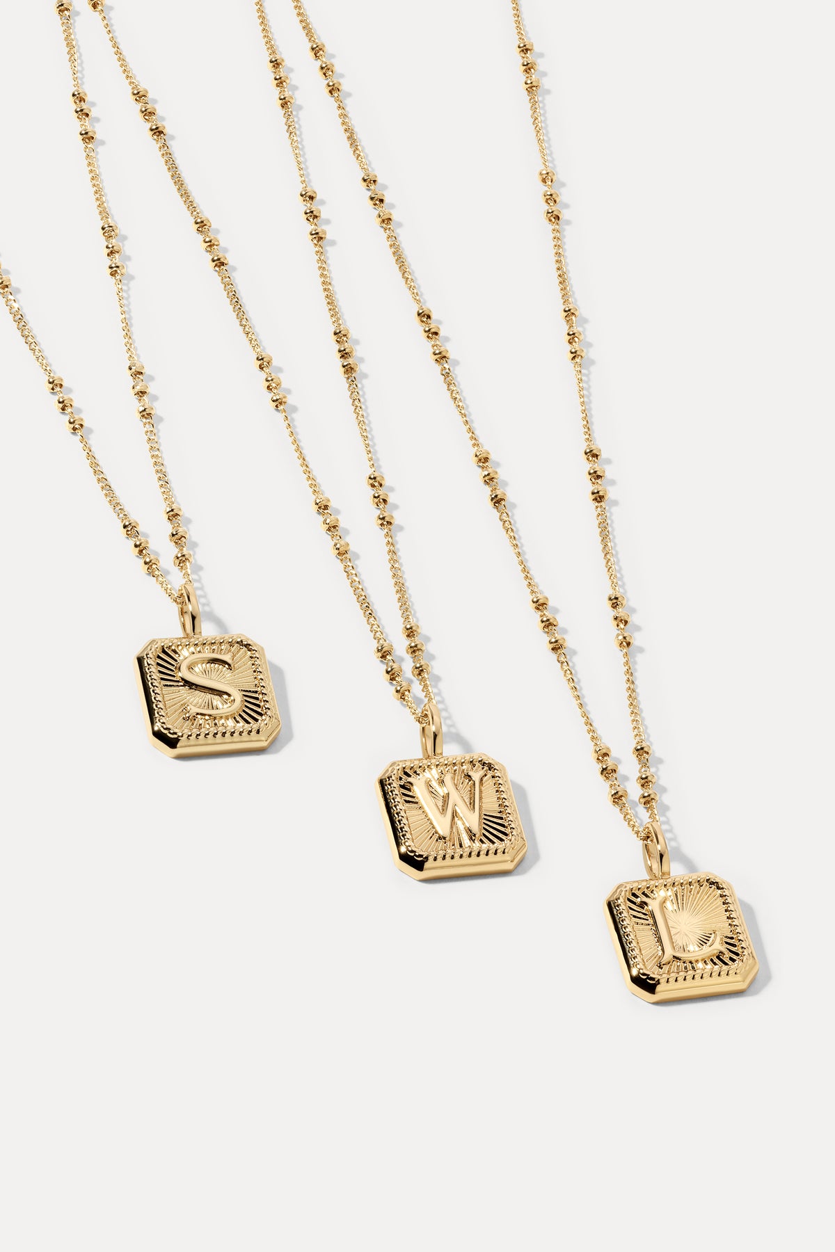Gold initial letter pendant attached to a gold satellite chain displayed against a plain white background.