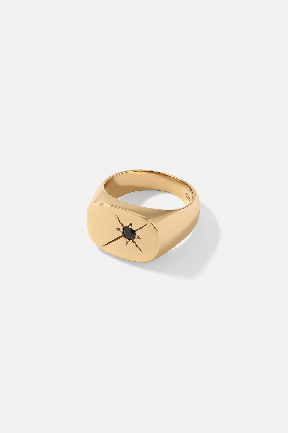 Studio product shot of the gold Dean signet ring with a starburst-set black gem, on a white background.