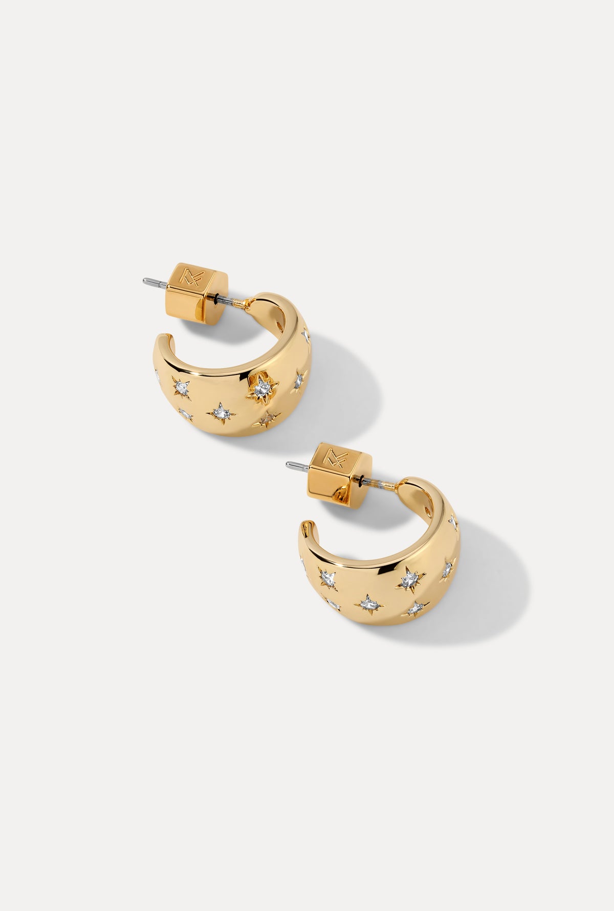 Pair of gold Lunette Huggies with starburst cubic zirconia settings on white background.