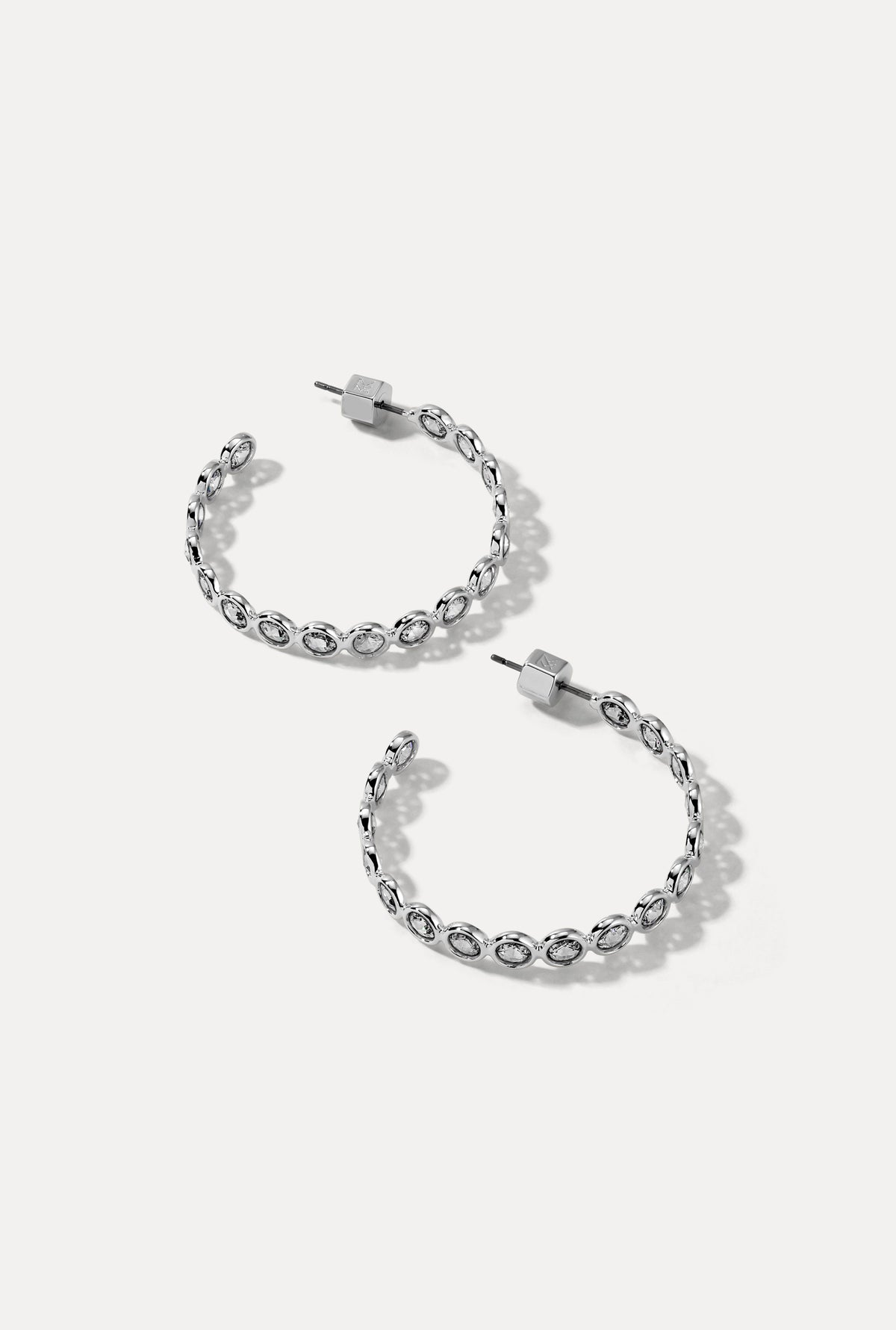 Pair of silver Lynda Hoops with bezel-set cubic zirconia stones on white background.