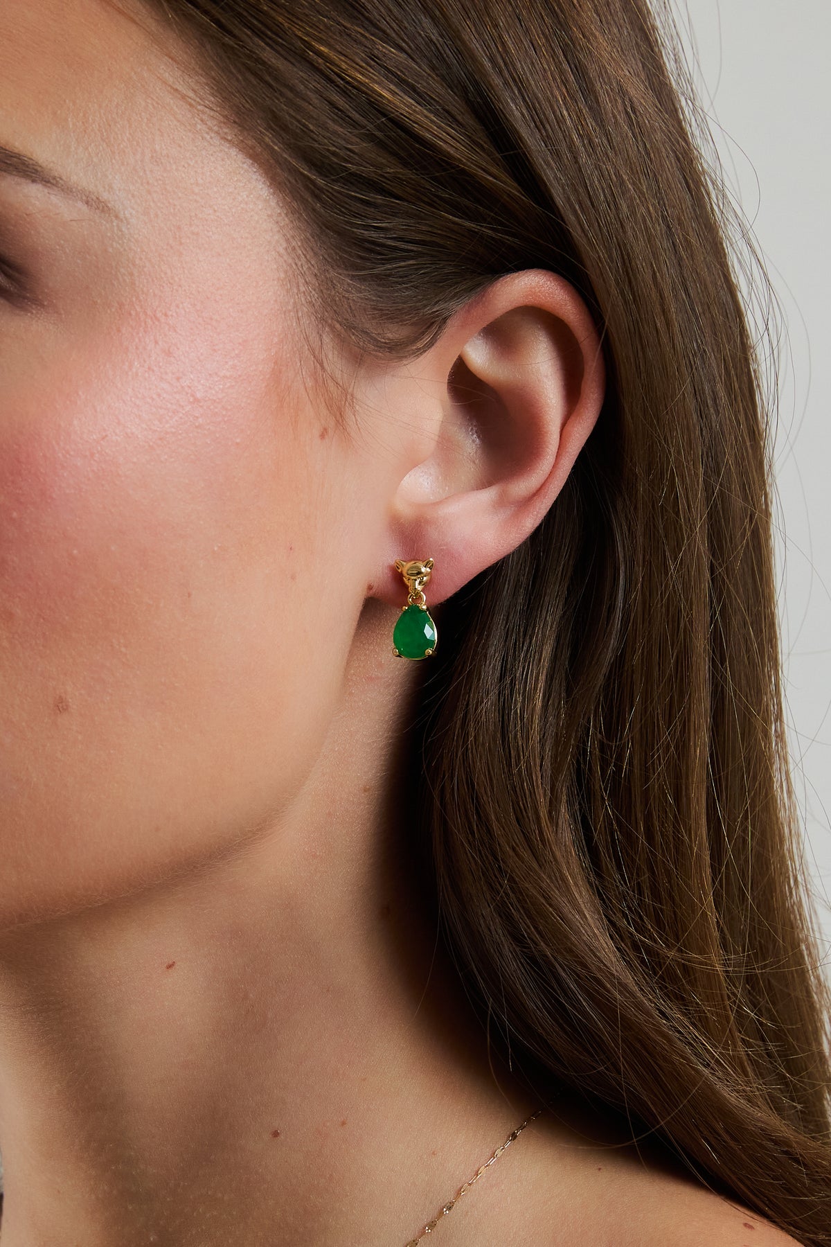 Model wearing gold Panther Emerald drop earring with green teardrop gem, featuring sculpted panther stud.