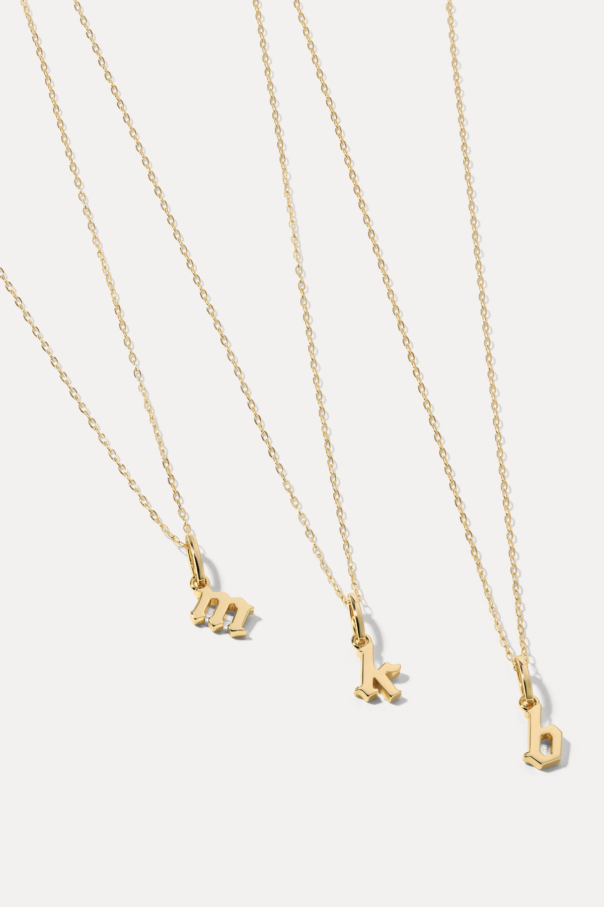 Gold delicate initial letter pendant attached to a thin gold chain displayed against a plain white background.