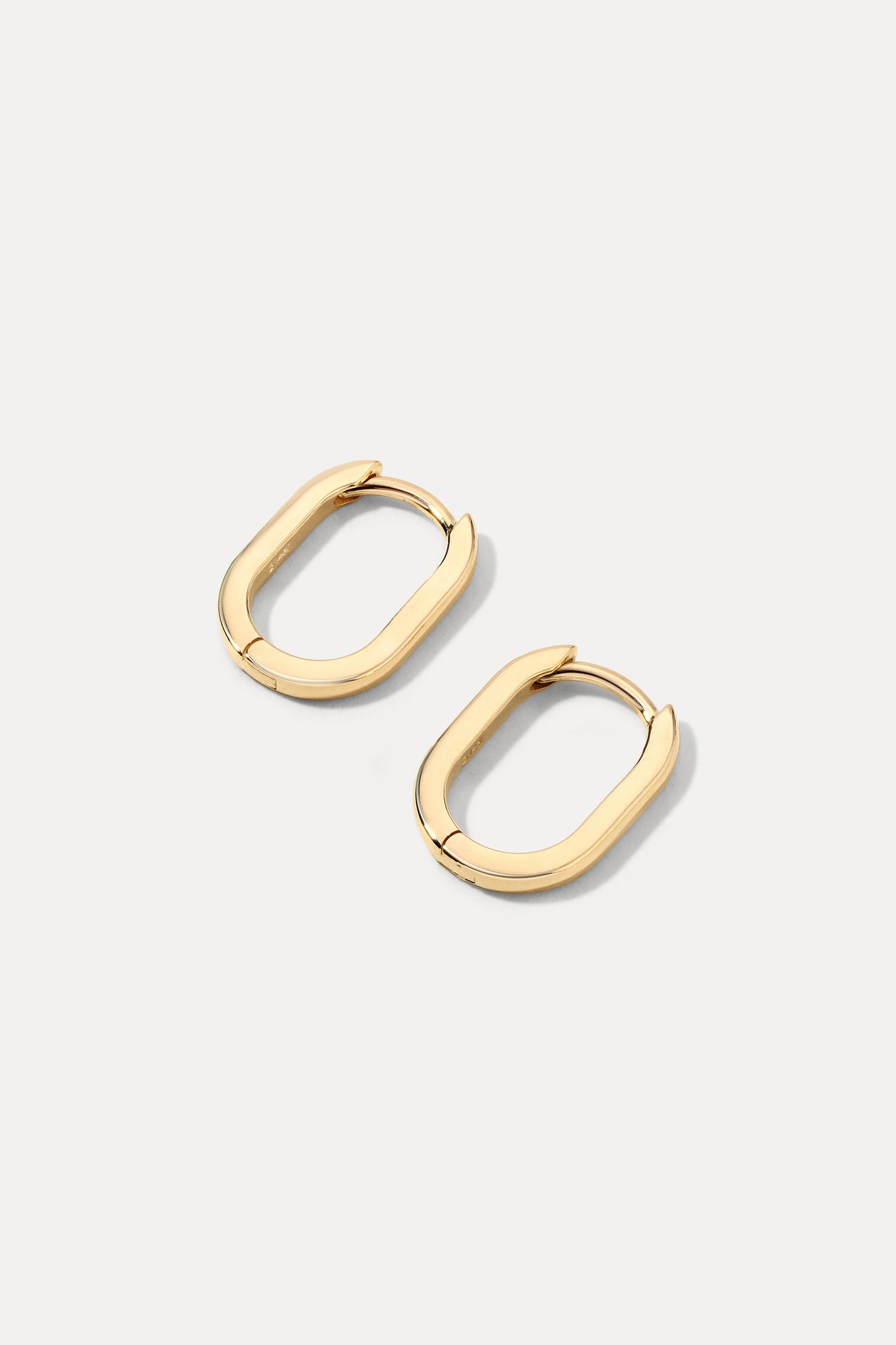 Pair of 14K gold petite oval huggie hoop earrings displayed on a plain white background.