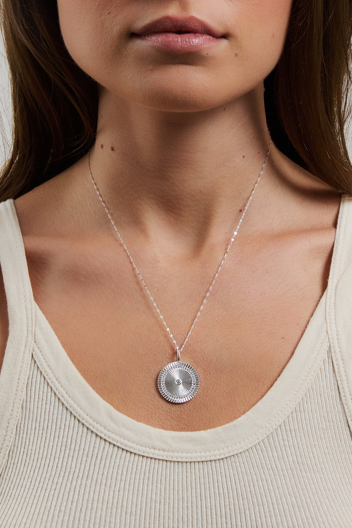 Close-up of model wearing silver Solara Charm medallion on nora chain in a cream ribbed top.
