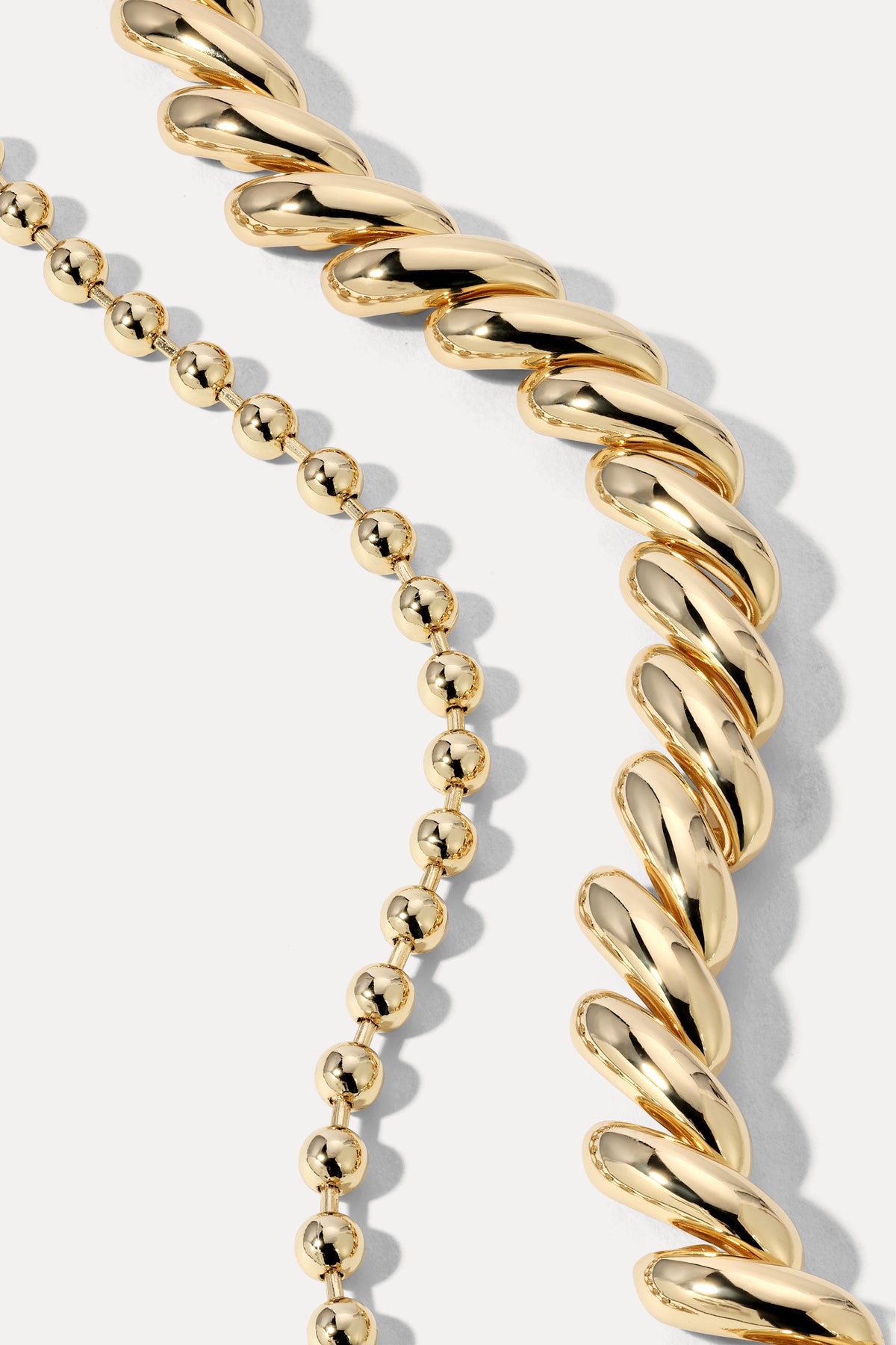 Gold layered bracelet stack combining ball chain and curb chain links on a plain white background.